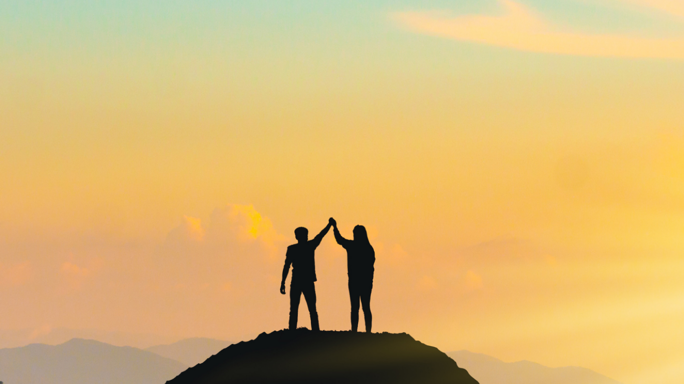 Two people standing on a mountain top holding their hands up in the air.